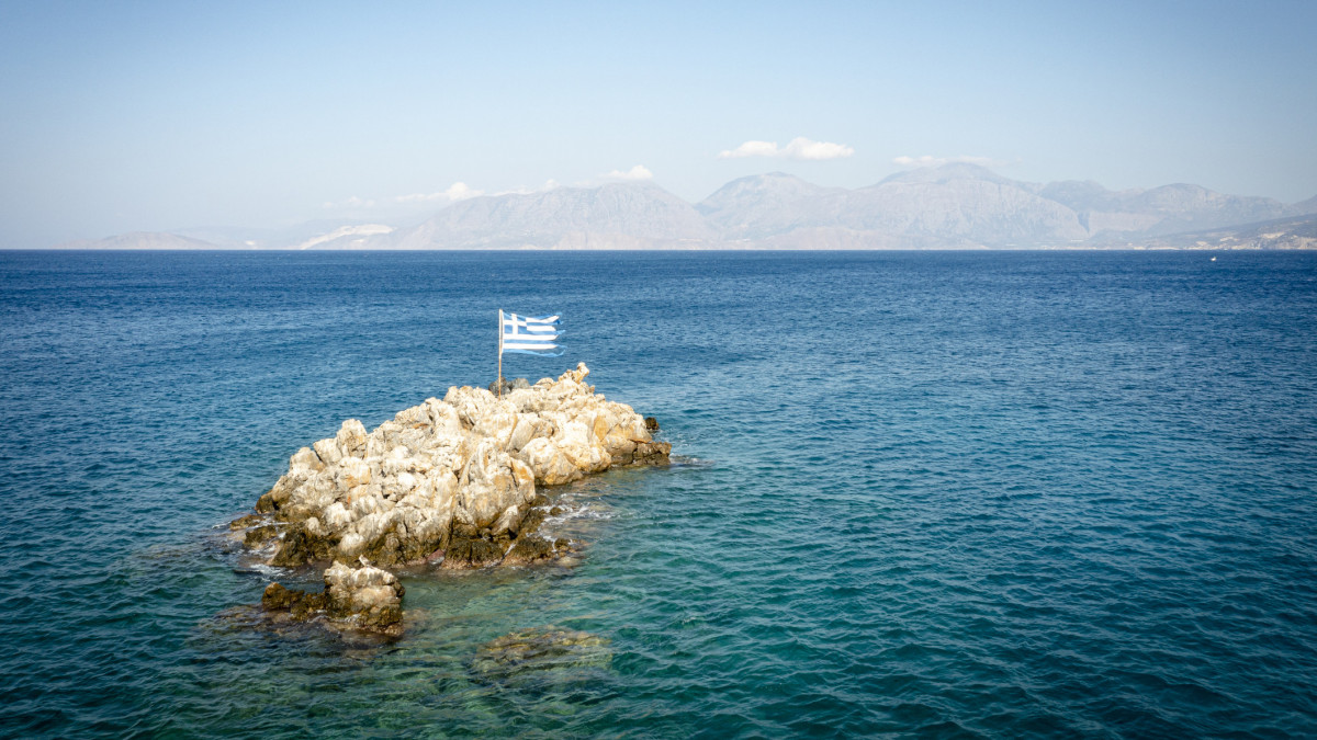 Rock with Greek flag in the middle of the crystal clear sea, Almyros Beach, Mirabella bay, Agios Nikolaos, Crete, Greece
