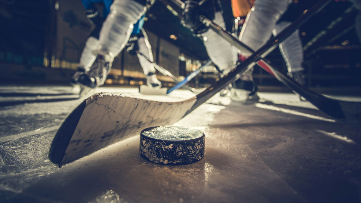 Close up of hockey puck and stick during a match with players in the background.