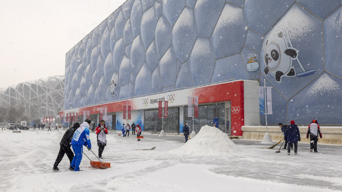 Peking, 2022. február 13.Önkéntesek havat lapátolnak a 2022-es pekingi téli olimpia curlingversenyeinek otthont adó Nemzeti Vízi Központ bejárata előtt 2022. február 13-án. A kínai fővárosban február 4-20. között rendezik a 2022-es téli ötkarikás játékokat.
