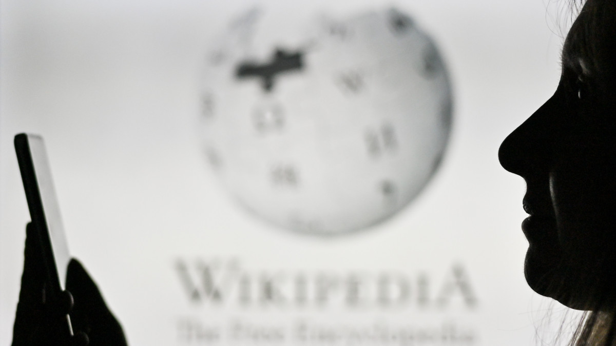 An image of a woman holding a cell phone in front of the Wikipedia logo displayed on a computer screen.On Tuesday, January 12, 2021, in Edmonton, Alberta, Canada. (Photo by Artur Widak/NurPhoto via Getty Images)