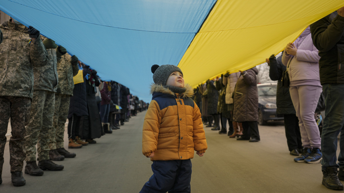 Ukrán kisgyerek áll a nemzeti egység napja alkalmából kifeszített 200 méteres nemzeti zászló alatt a kijevi Olimpiai Stadionban 2022. február 16-án.
