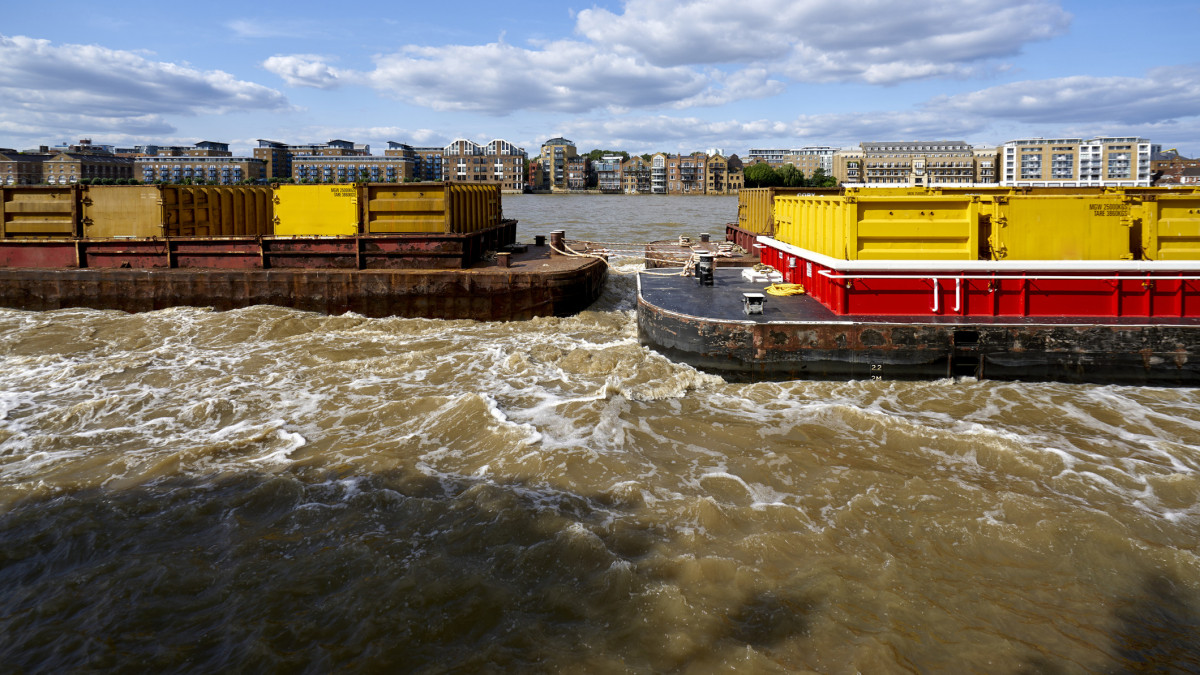 Tugboats pulling vessels of London containers of refuse and garbage eastwards on the River Thames East London UK