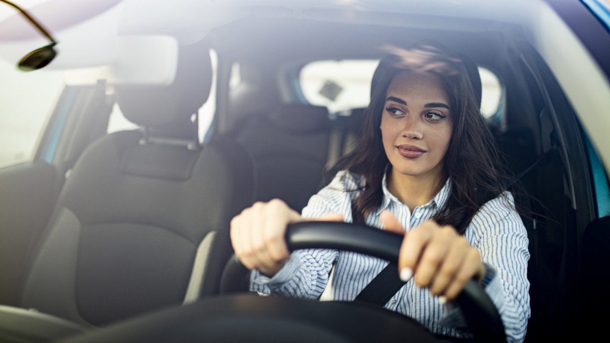 Happy woman driving a car and smiling. Cute young success happy brunette woman is driving a car. Portrait of happy female driver steering car with safety belt