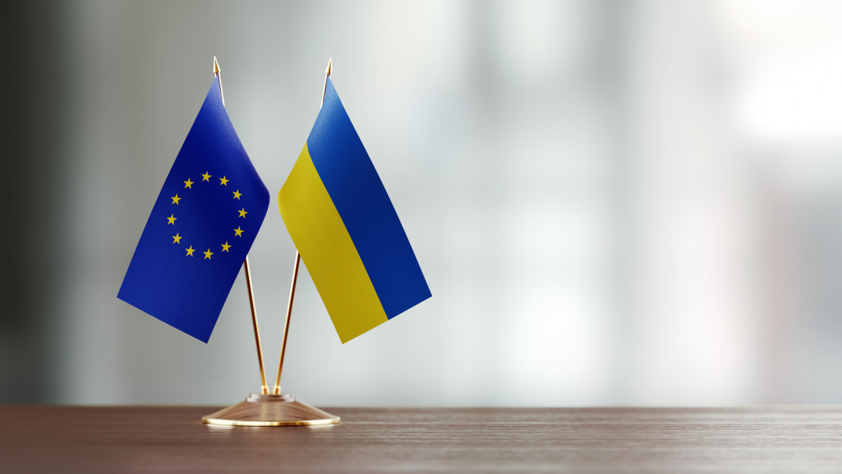 European Union and Ukrainian flag pair on desk over defocused background. Horizontal composition with copy space and selective focus.