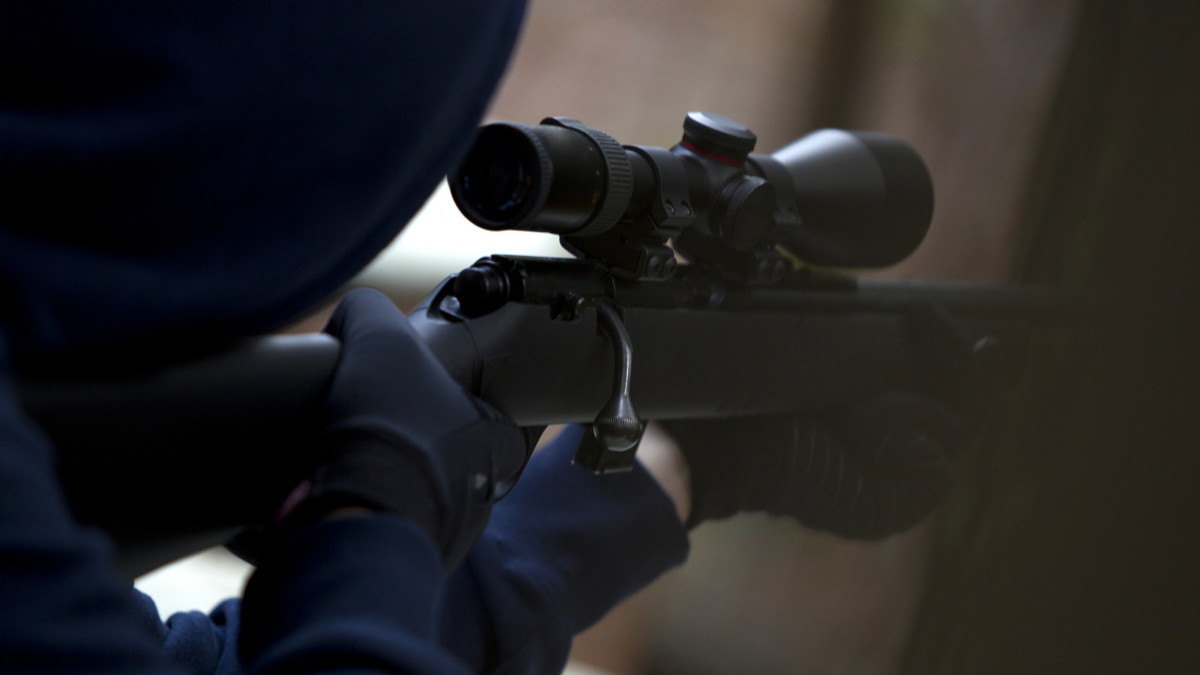 Person taking aim with rifle, shallow depth of field, slight grain due to low light.