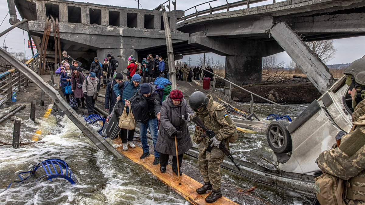 Katonák segítenek a Kijev közelében lévő Irpinyből menekülő embereknek átkelni egy orosz légicsapásban lerombolt híd alatt kialakított átkelőn az Irpiny folyón 2022. március 7-én. Vlagyimir Putyin orosz elnök február 24-én rendelte el katonai művelet végrehajtását Ukrajnában.