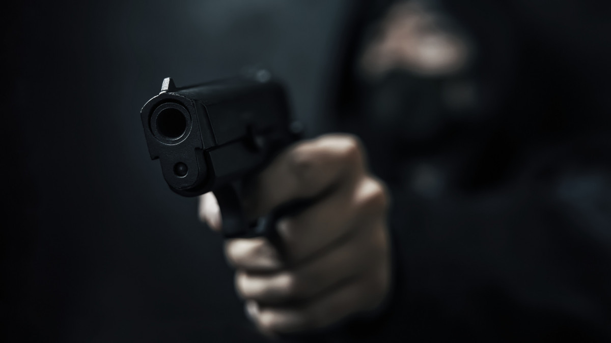 Masked robber with gun aiming into camera. Man in hood threatens with firearm. Weapon in persons hands. Murderer or armed thief. Criminal with pistol.