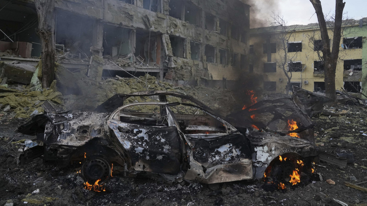 Égő autó a bombatámadásban megrongálódott mariupoli gyermekkórháznál 2022. március 9-én. Vlagyimir Putyin orosz elnök február 24-én rendelte el katonai művelet végrehajtását Ukrajnában.