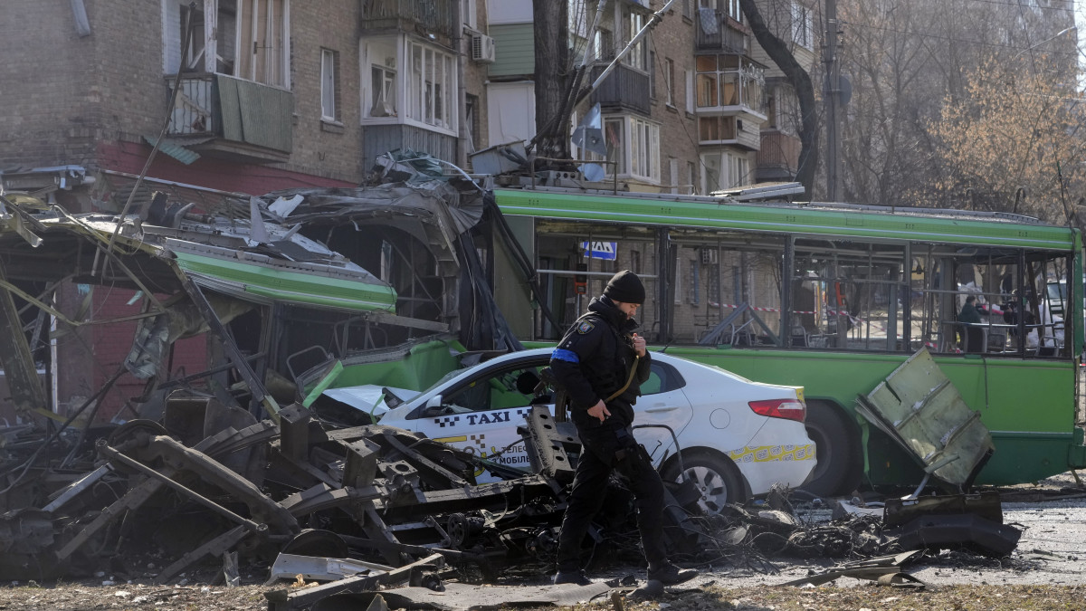 Ukrán katona halad el bombatámadásban megrongálódott trolibusz és taxi előtt Kijevben 2022. márciius 14-én. Vlagyimir Putyin orosz elnök február 24-én rendelte el katonai művelet végrehajtását Ukrajnában.
