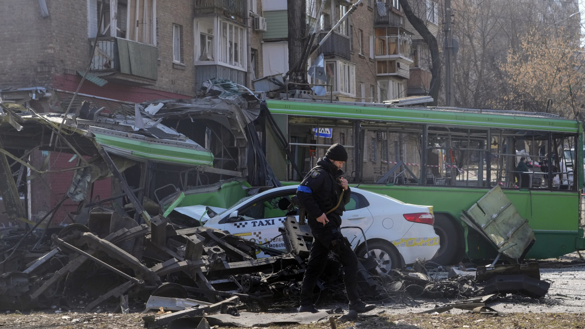 Ukrán katona halad el bombatámadásban megrongálódott trolibusz és taxi előtt Kijevben 2022. márciius 14-én. Vlagyimir Putyin orosz elnök február 24-én rendelte el katonai művelet végrehajtását Ukrajnában.