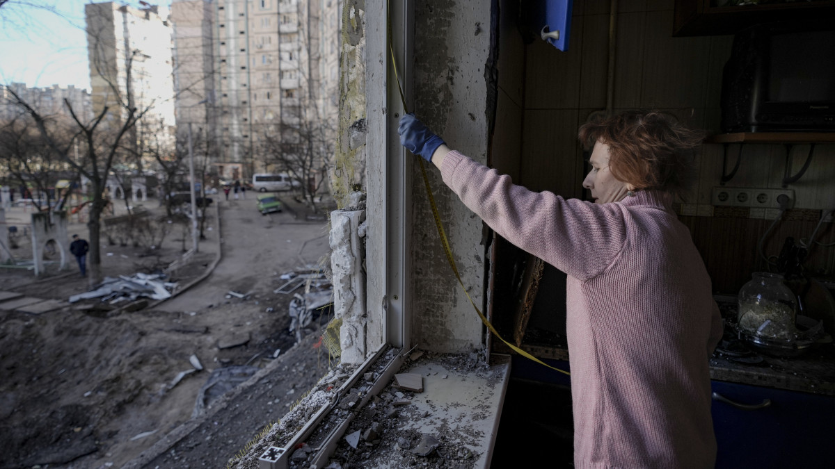 A tüzérségi támadásban súlyosan megrongálódott lakásának ablakát méri egy nő Kijevben 2022. március 21-én. Vlagyimir Putyin orosz elnök február 24-én rendelte el katonai művelet végrehajtását Ukrajnában.