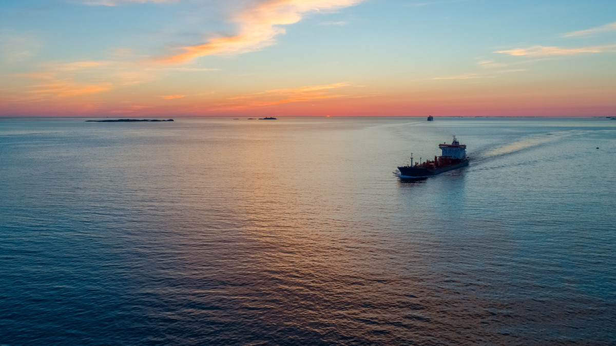 A tank ship can be seen sailing in the waters of Austrheim, Norway against a stunning sunset backdrop. Shot from a drone on a summer evening.