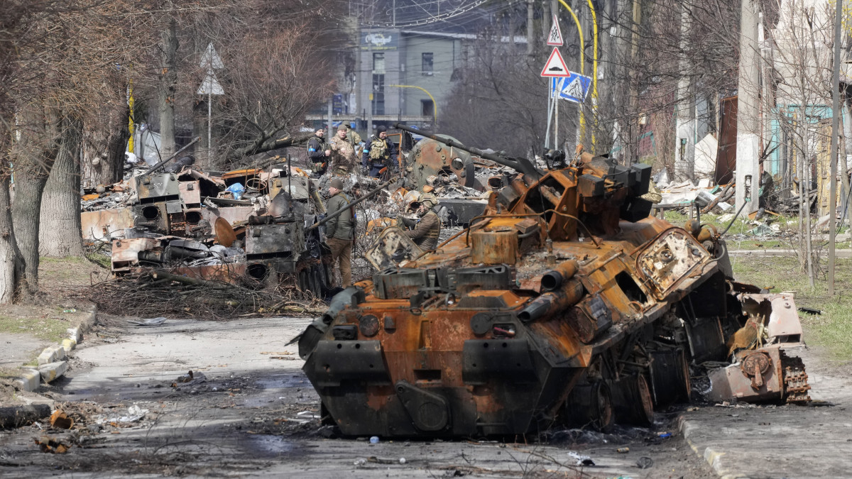 Ukrán katonák egy megrongálódott orosz katonai jármű mellett a Kijev melletti Bucsában 2022. április 4-én.