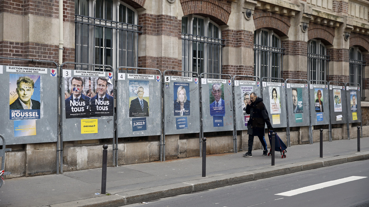 PARIS, FRANCE - APRIL 09: A man walks past official campaign posters of the candidates for the 2022 presidential election displayed on billboards next to a polling station on April 09, 2022 in Paris, France. According to latest polls, Marine Le Pen is credited with 25 % and Emanuel Macron is credited with 26 % of voting intentions in the first round of the presidential election. On Sundays April 10 and 24, 2022, 47.9 million voters are called upon to vote to elect the next President of the French Fifth Republic. (Photo by Chesnot/Getty Images)