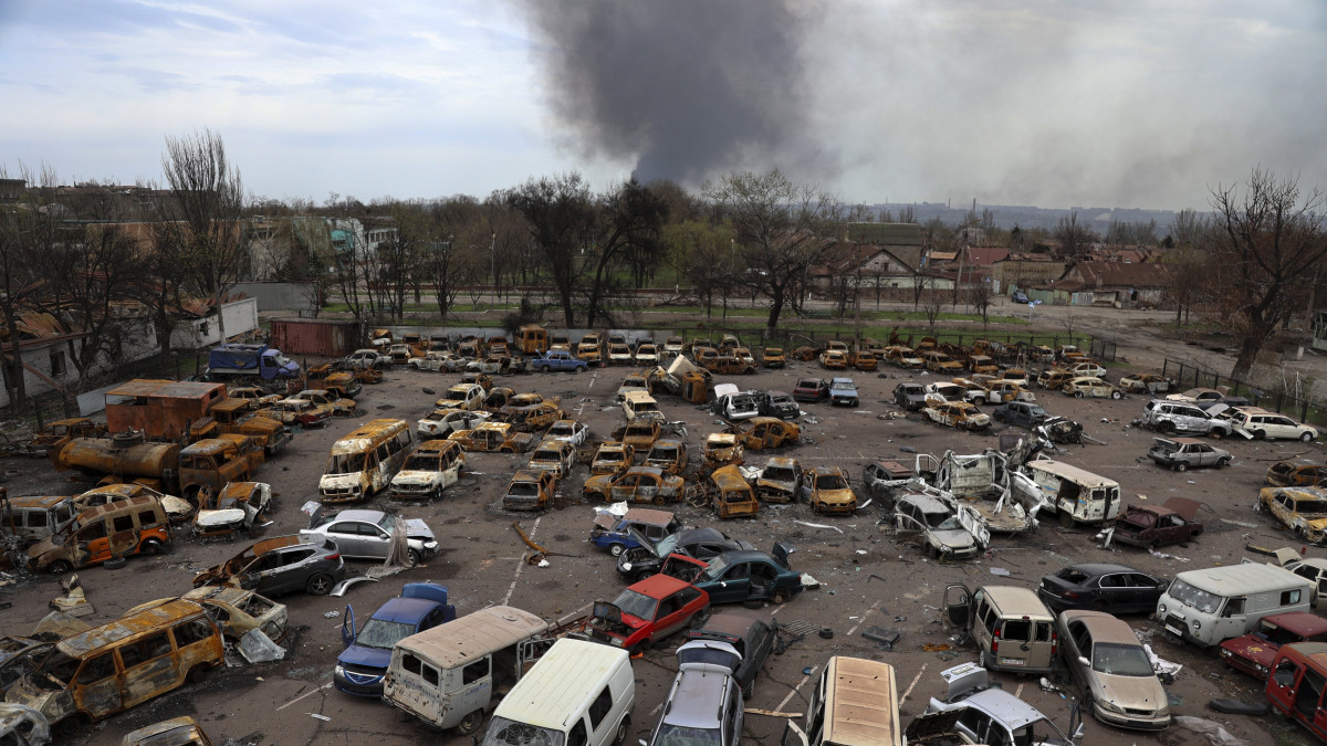 Megrongálódott és kiégett járművek az Iljics Acél- és Vasművek területén, miközben füst száll fel az Azovsztal acélgyár területéről Mariupolban 2022. április 18-án.