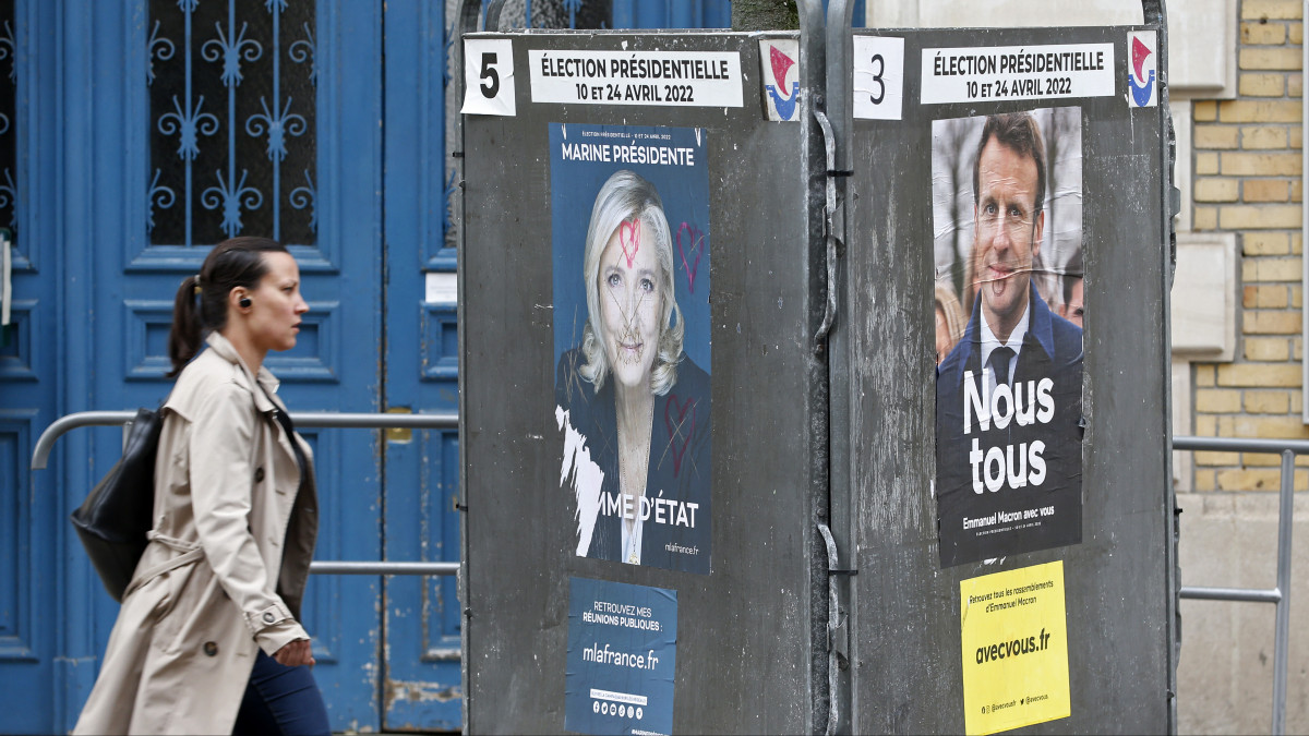 PARIS, FRANCE - APRIL 13: A woman walks past damaged official campaign posters of Marine Le Pen, leader of the far-right Rassemblement national (RN) party and French President Emmanuel Macron La RĂŠpublique en marche (LREM), candidates in the 2022 French presidential election, displayed on billboards next to a polling station on April 13, 2022 in Paris, France. French President Emmanuel Macron candidate for re-election, obtained 27.6% of the vote and Marine Le Pen obtained 23.4% of the vote in the first round of the presidential election. Emmanuel Macron and Marine Le Pen were both qualified on Sunday April 10th for Frances Presidential Election second round to be held on April 24. This is the third bid at president for Marine Le Pen, who placed third in the 2012 campaign and was defeated in the 2017 runoff by current President Emmanuel Macron. (Photo by Chesnot/Getty Images)