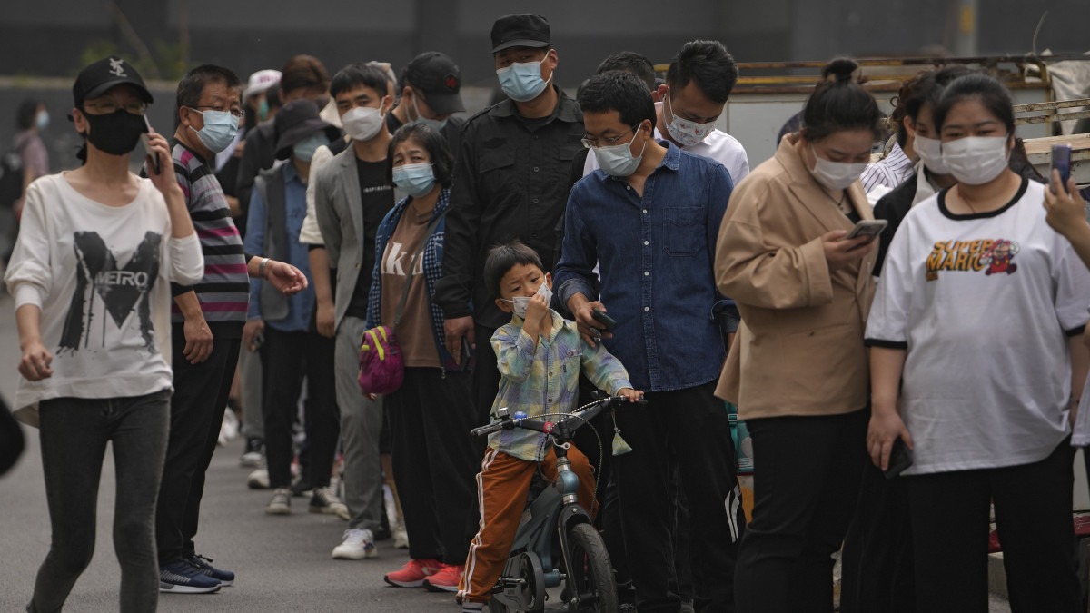 Koronavírus-tesztelésre váró, védőmaszkot viselő emberek Peking üzleti negyedében 2022. április 25-én. A kínai főváros egyes részein tömeges tesztelést kezdtek meg, miután 23-án 21 új esetet azonosítottak. Minthogy az új esetek egy részét a város fontos üzleti központjának számító, keleti Csaojang kerületben azonosították, a kerület lakóit és az ott dolgozókat három körben vetik alá nukleinsavas vírustesztelésnek.