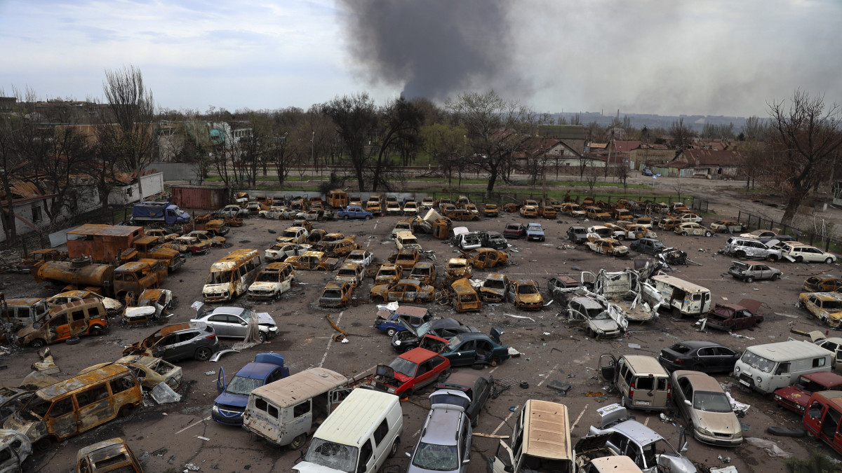 Megrongálódott és kiégett járművek az Iljics Acél- és Vasművek területén, miközben füst száll fel az Azovsztal acélgyár területéről Mariupolban 2022. április 18-án.
