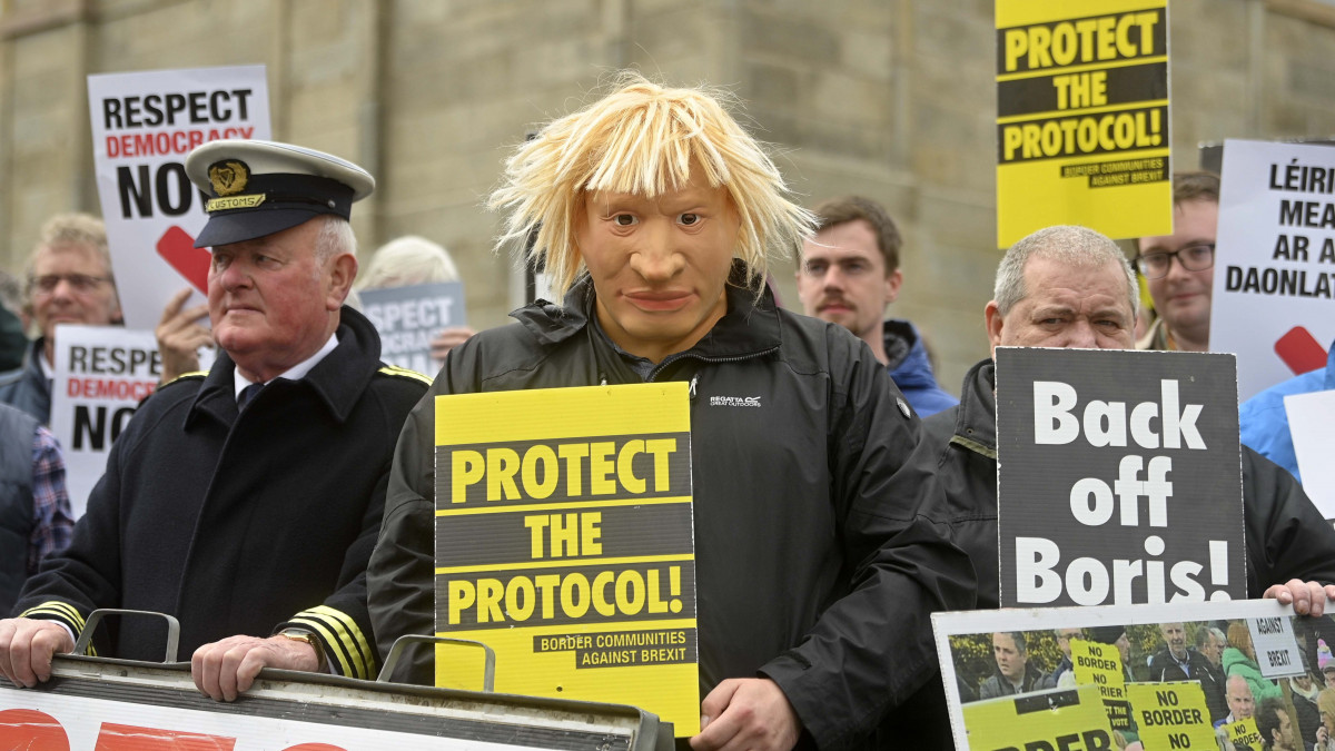 Boris Johnson brit kormányfőt ábrázoló gúnymaszkot visel egy északír tüntető a kormányfő látogatása idején a Belfast közelében levő Hillsborough kastélyánál 2022. május 16-án, tizenegy nappal a tartományi parlamenti választások után. Johnson a brexit-megállapodás részét képező észak-írországi protokollról tárgyal a kormányalakítással megbízott helyi pártok vezetőivel.