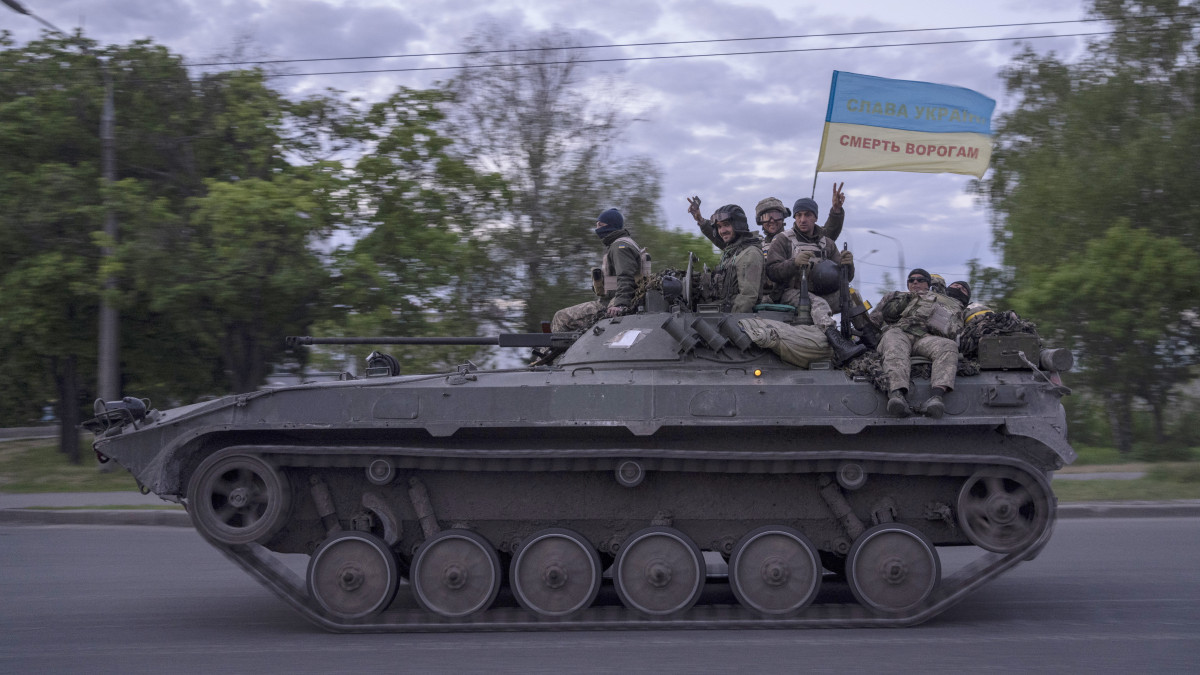 Tank tetején ülő ukrán katonák Dicsőség Ukrajnának és Halál az ellenségre feliratú ukrán zászlót lobogtatnak a kelet-ukrajnai Harkiv megyében 2022. május 17-én.