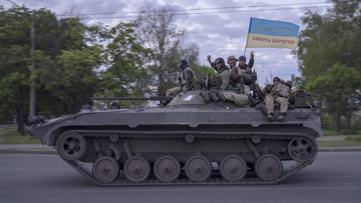 Tank tetején ülő ukrán katonák Dicsőség Ukrajnának és Halál az ellenségre feliratú ukrán zászlót lobogtatnak a kelet-ukrajnai Harkiv megyében 2022. május 17-én.