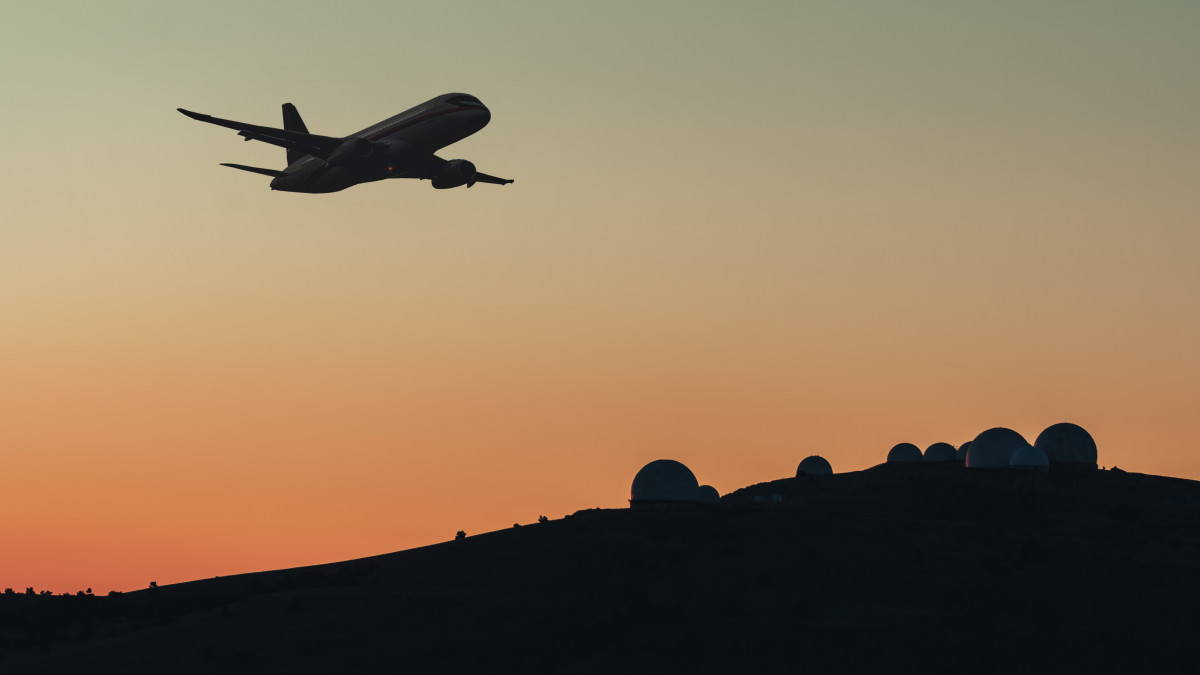 Military radio radars with satellite antenna searches and detects the silhouette of a commercial or transport jet airplane flying in the mountains. Station of surveillance at the military base carries control and intelligence service of the airspace in the dark sky at night.