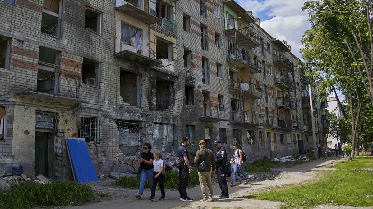 Járókelők orosz támadásokban megrongálódott lakóépületek mellett Harkiv külvárosában 2022. május 25-én.