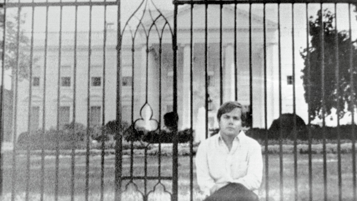 (Original Caption) Washington, D.C.: This photo acquired by UPI shows John Hinckley Jr., as he sits on fence wall in front of the White House. Hinckley is accused as the attempted assassin of President Ronald Reagan. The picture is undated but believed to have been taken within the past year.