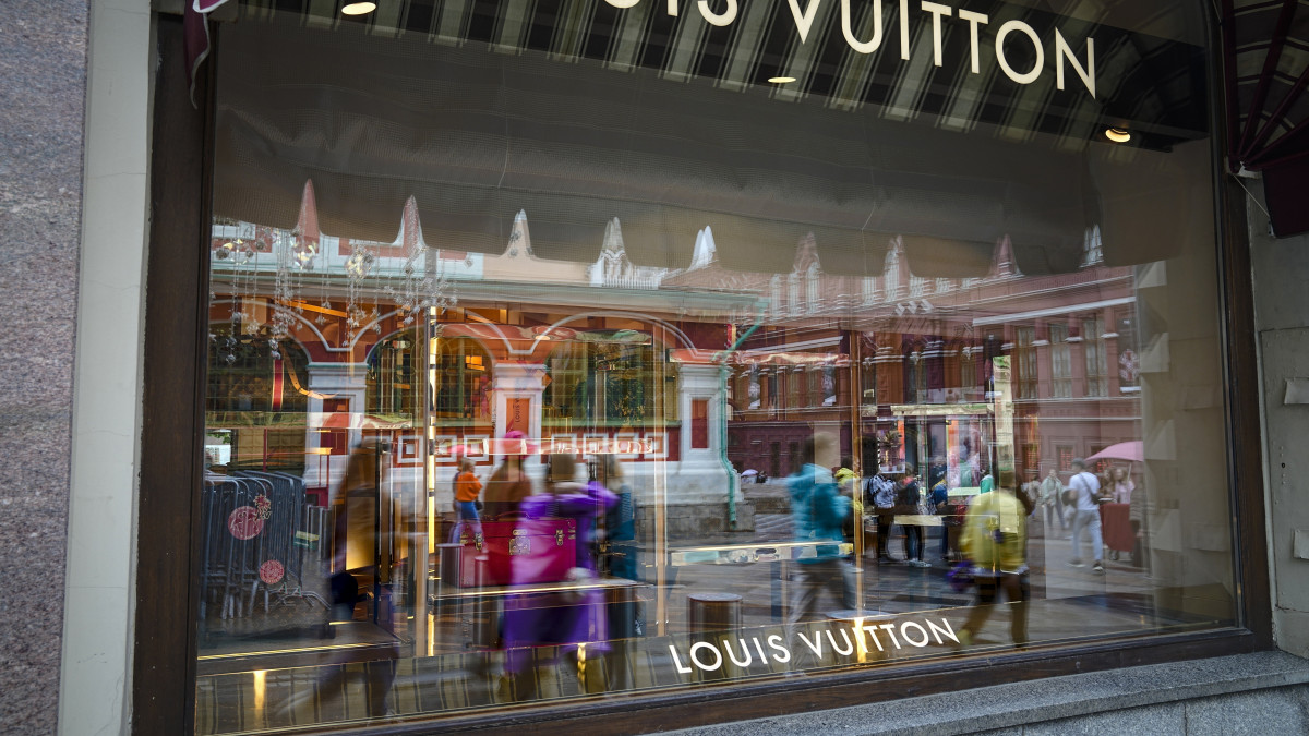 A moszkvai GUM áruház bezárt Louis Vuitton-üzletének kirakatüvegén tükröződnek járókelők 2022. május 31-én. A francia luxus divatcég több más nyugati vállalathoz hasonlóan kivonult az orosz piacról az Ukrajna ellen indított orosz háború elleni tiltakozásul.