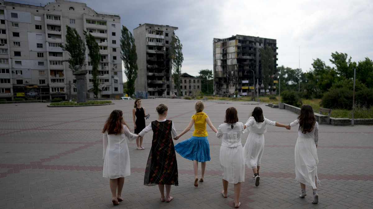 Lányok táncolnak az orosz támadásokban megsemmisült épületek maradványaival a háttérben a Kijev közelében fekvő Borogyankában 2022. június 21-én.