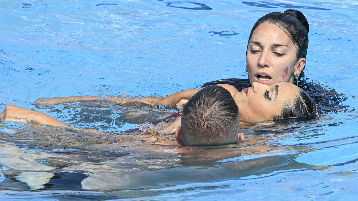 A gyakorlata befejezése után elájult amerikai Anita Alvarezt edzője, Andrea Fuentes és egy segítő hozza ki a medencéből a szinkronúszók egyéni szabadprogram versenyének döntőjében a vizes világbajnokságon a margitszigeti Hajós Alfréd Nemzeti Sportuszodában 2022. június 22-én.