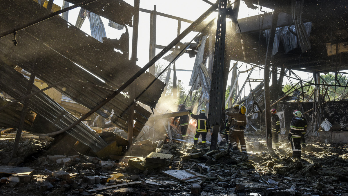 Bevásárlóközpont romjai között tűzoltók 2022. június 28-án, az ukrajnai Kremencsukot érő orosz rakétatámadás másnapján.