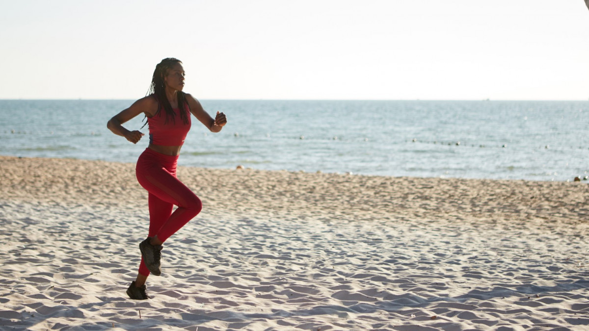 Fit young Black woman in red top and leggins jogging on sandy beach