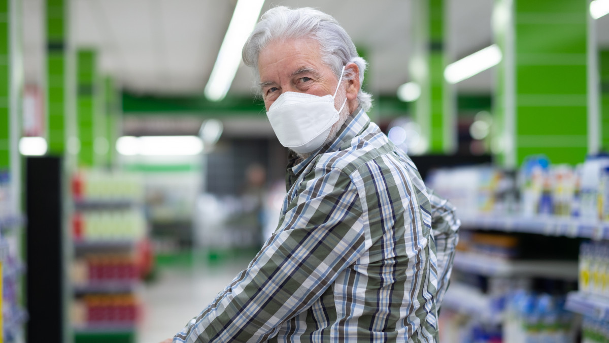 Senior man wearing ffp2 mask to avoid contagion by covid 19 coronavirus pushing cart in supermarket for shopping
