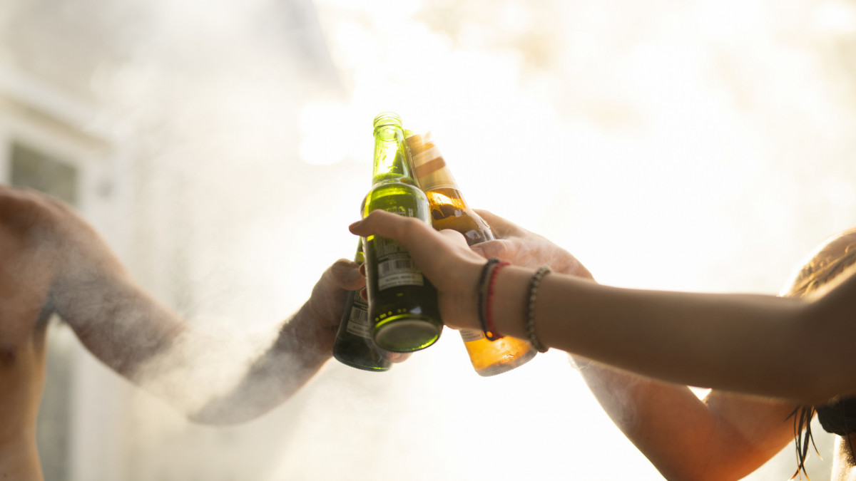 Cropped image of friend toasting beer bottles. Close-up of hands are surrounded by smoke. Friends are enjoying summer vacation at resort. Celebrations and toasting during summer vacation over barbecue smoke.