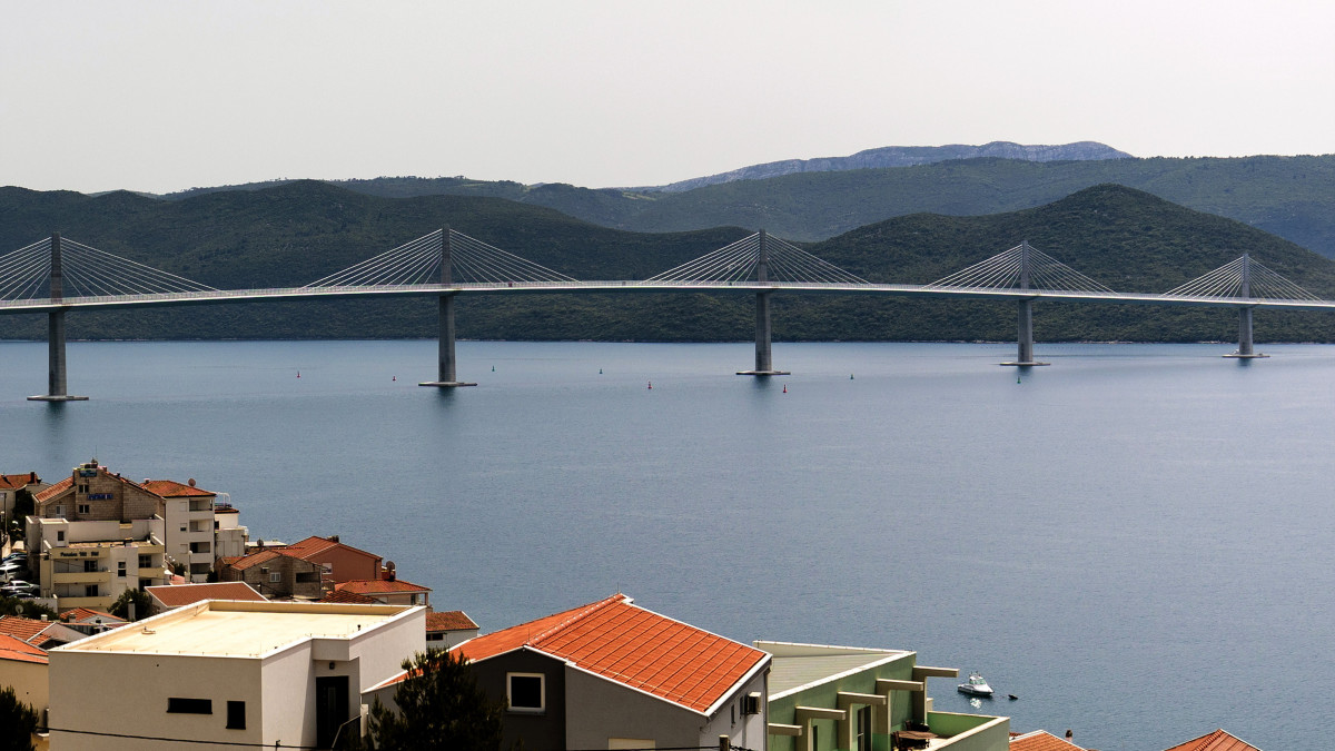 2022. június 30-án készített kép a Peljesac hídról a horvátországi Komarna közelében. A 420 millió eurós költséggel a kínai China Road and Bridge Corporation (CRBC) által megépített híd a szárazföld és a Peljesac-félsziget között ível át 55 méter magasságban a tengeröböl fölött, és így megteremti az összeköttetést Bosznia-Hercegovina tengerpartjának elkerülésével az attól északra és délre húzódó, Horvátországhoz tartozó Adria-parti területek között. A hidat 2022. július 26-án adják át.