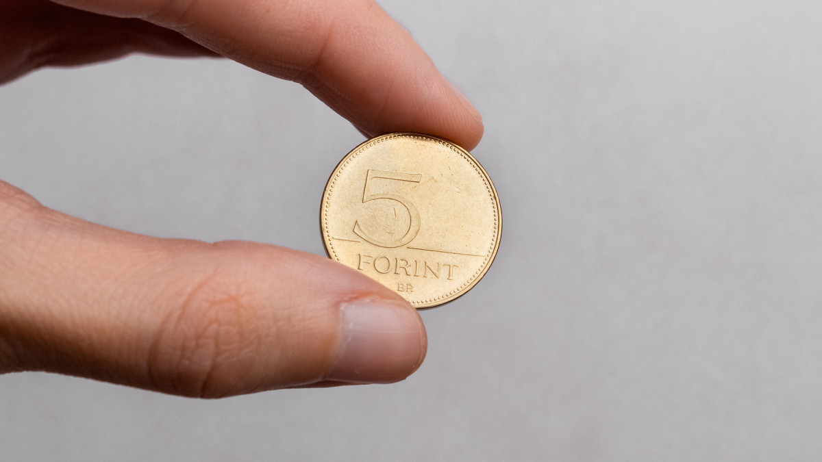 A hand holds a Hungarian five forint coin on a white background close-up.