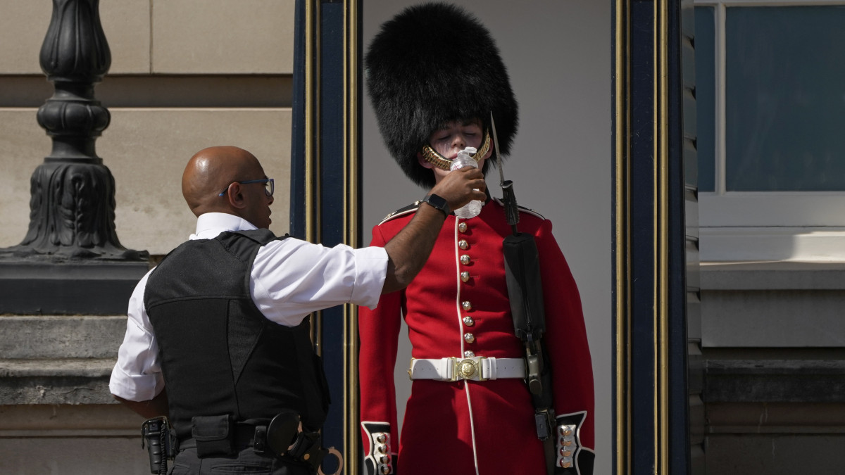 Szolgálatban levő brit palotaőrt itat egy rendőr a londoni Buckingham-palota kapujában 2022. július 18-án, amikor a brit hatóságok a legmagasabb szintű időjárási veszélyhelyzetet hirdettek, mivel Anglia déli és középső térségeiben a napokban 40 fok körüli hőség várható. Először adtak ki négyes szintű, vörös riasztást a rendkívüli hőség miatt Nagy-Britanniában, ahol Cambridge-ben mérték az eddigi rekordmeleget, 38,7 fokot 2019. július 25-én.