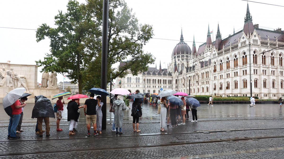 Az augusztus 20-ai nemzeti ünnep alkalmából rendezett nyílt napra érkező látogatók állnak sorban esernyőket tartva az Országház előtt 2022. augusztus 20-án. A nemzeti ünnepen ingyenesen tekinthető meg a díszlépcsőház, a Kupolacsarnok és a Szent Korona.