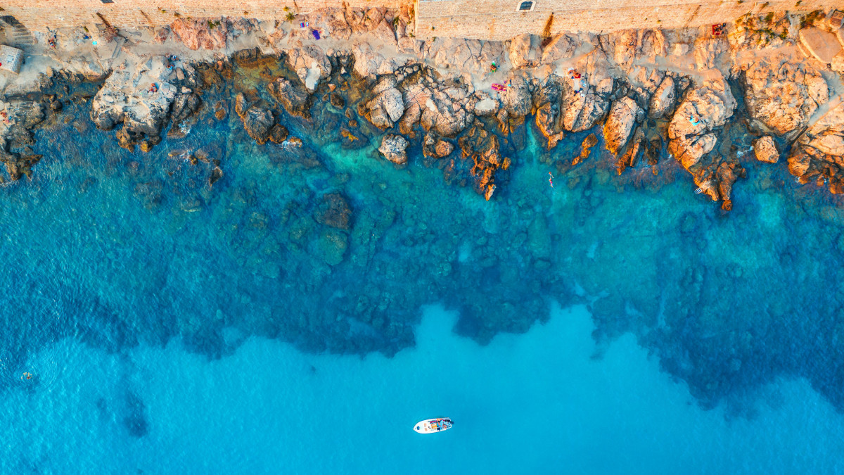 Aerial view of beach with stones and rocks, alone boat in adriatic sea at sunset in summer. Top view of yacht in transparent blue water. Travel in Croatia. Nature background. Landscape with ocean