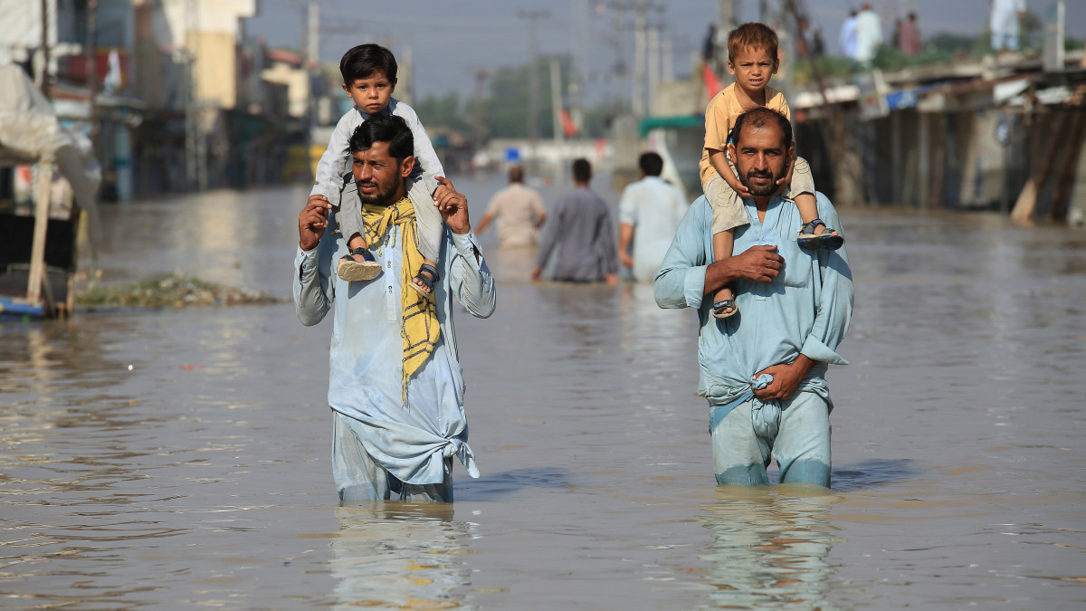 Térdig érő vízben gyalogolnak emberek az árvíz sújtotta pakisztáni Novserában 2022. augusztus 29-én. Pakisztánban a június közepe óta tartó árvizekben 1033 ember életét vesztette, a monszunesők okozta áradások miatt mintegy 33 millió embernek kellett elhagynia lakóhelyét.
