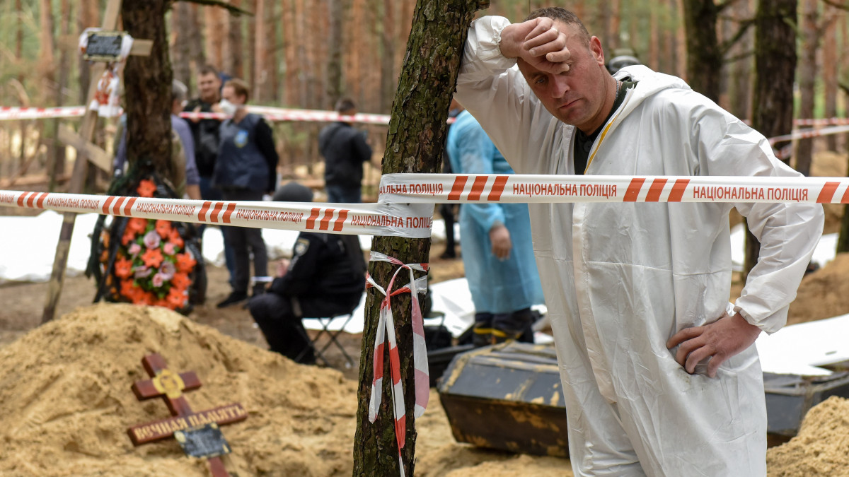Fának dőlve tart pihenőt az azonosítatlan áldozatok földi maradványait exhumáló csoport egyik tagja a kelet-ukrajnai Harkiv megyében levő Izjumnál 2022. szeptember 16-án, a tömegsír felfedezésének másnapján. Az ukrán hatóságok több mint 440 egyenként elásott holttestet hantoltak ki az orosz erőktől nemrégiben visszafoglalt város melletti erdőben.