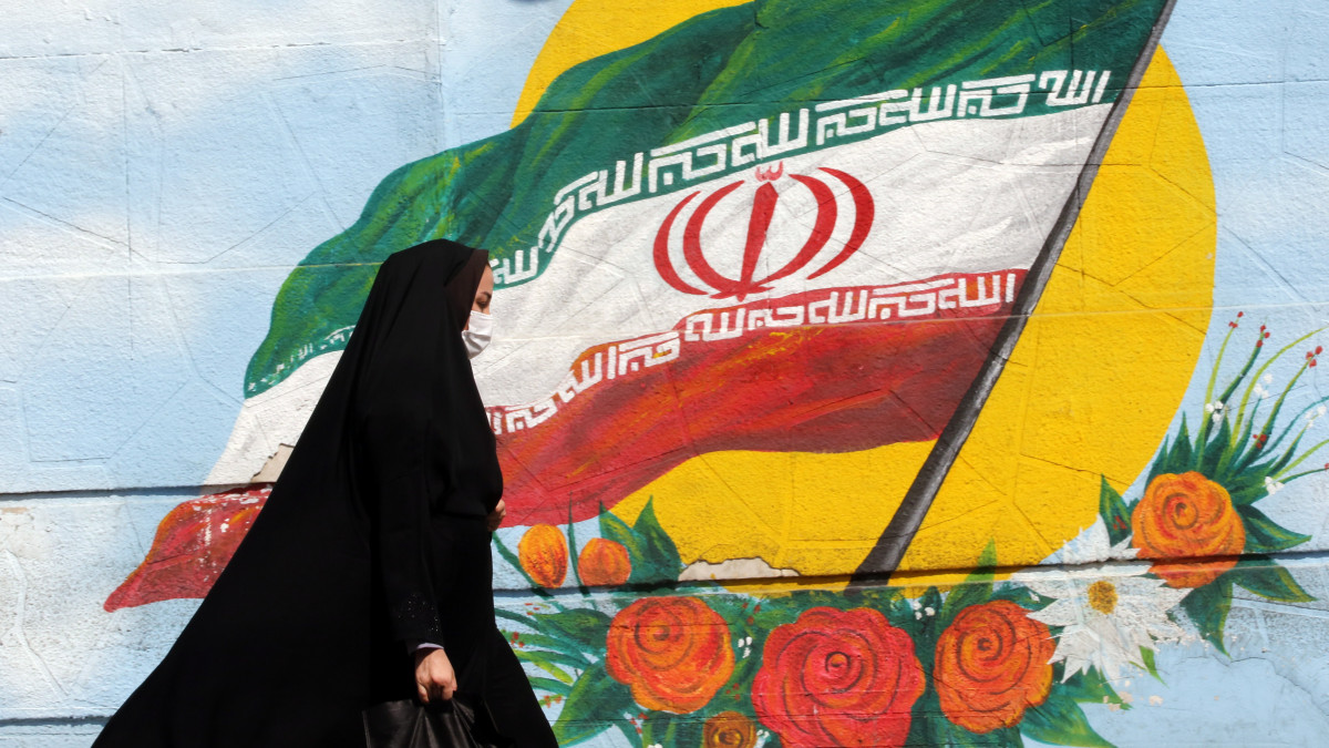 A koronavírus-járvány miatt védőmaszkot viselő nő halad el egy iráni zászlót ábrázoló falfestmény mellett Teheránban 2021. augusztus 9-én. Az iráni egészségügyi minisztérium közlése szerint az országban az elmúlt napokban rekordot döntött a koronavírus-fertőzöttek és a fertőzés szövődményei miatt elhunyt emberek száma.