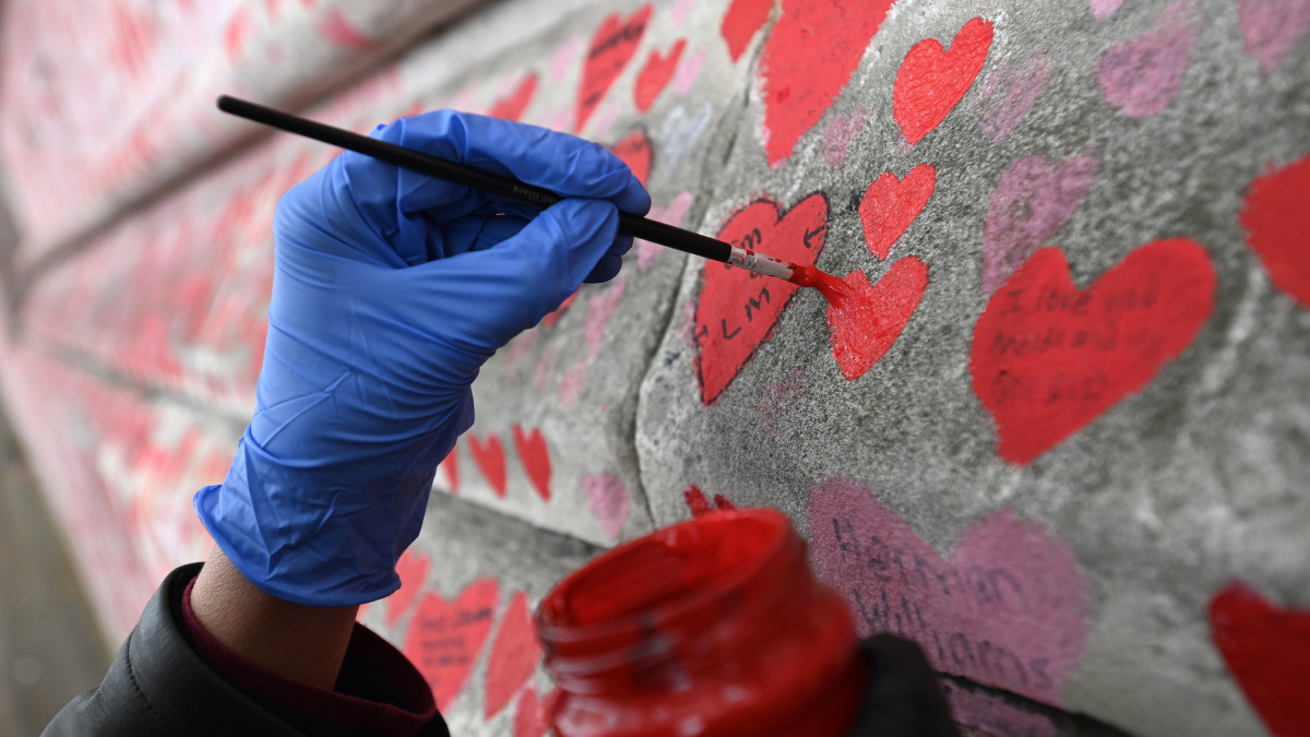 Elhunyt édesapja emlékére fest piros szívet egy nő a koronavírus-járvány brit áldozatai tiszteletére kialakított emlékfalra London belvárosában 2022. április 28-án. Nagy-Britanniában több mint 173 ezer áldozatot követelt eddig a 2019 végétől.