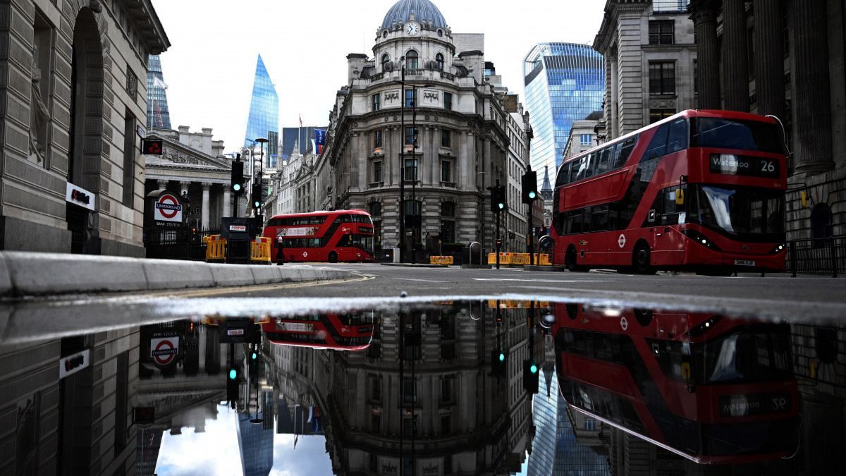A 2020. május 14-én készült, június 18-án közreadott képen piros buszok haladnak el a brit jegybank, a Bank of England épületénél London pénzügyi negyedében. Ezen a napon bejelentették, hogy a brit jegybank százmilliárd font pótlólagos likviditást juttat a brit gazdaságba az új koronavírus okozta járvány súlyos hatásainak enyhítése érdekében.