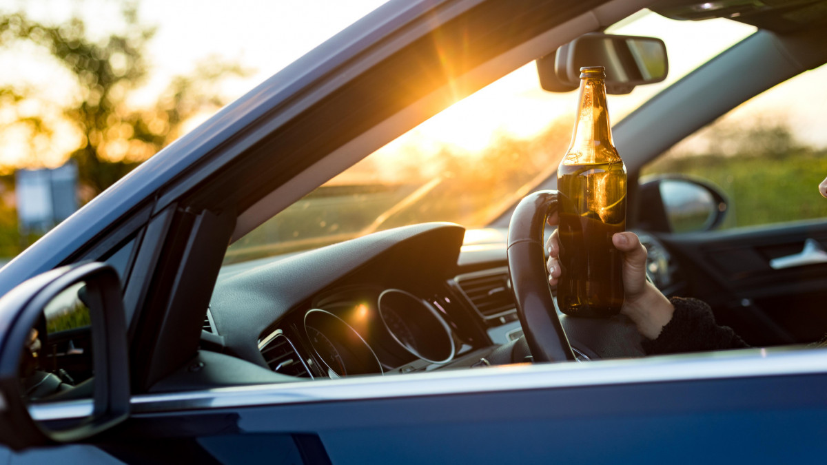 Young adult drinking beer while driving, she is going to a party.