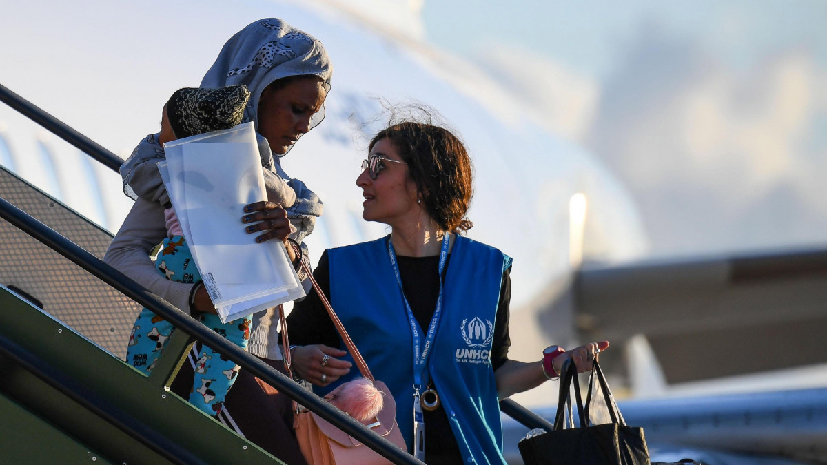 A líbiai Miszrátából elszállított menedékkérő érkezik gyermekével olasz katonai repülőgéppel a Róma melletti Pomezia Pratica di Mare légi támaszpontra, jobbról az ENSZ Menekültügyi Főbiztosságának munkatársa 2019. április 29-én. Olaszország 147 etiópiai, eritreai, szomáliai, szudáni és szíriai menedékkérőt evakuált Líbiából az ott fellángolt harcok miatt.
