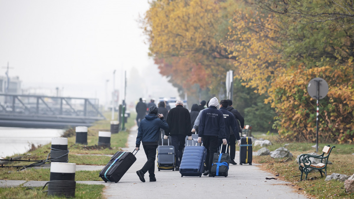 A németországi Passauból érkező utasok bőröndjeikkel gyalogolnak, miután leszálltak az őket szállító turistahajóról Bécs egyik kikötőjében 2021. október 28-án. A Dunán közlekedő hajó 178 utasából legalább 80-nak pozitív lett a koronavírustesztje, ezért mindenkinek a hajón kellett töltenie az éjszakát. Az utasokat valószínűleg busszal szállítják vissza.