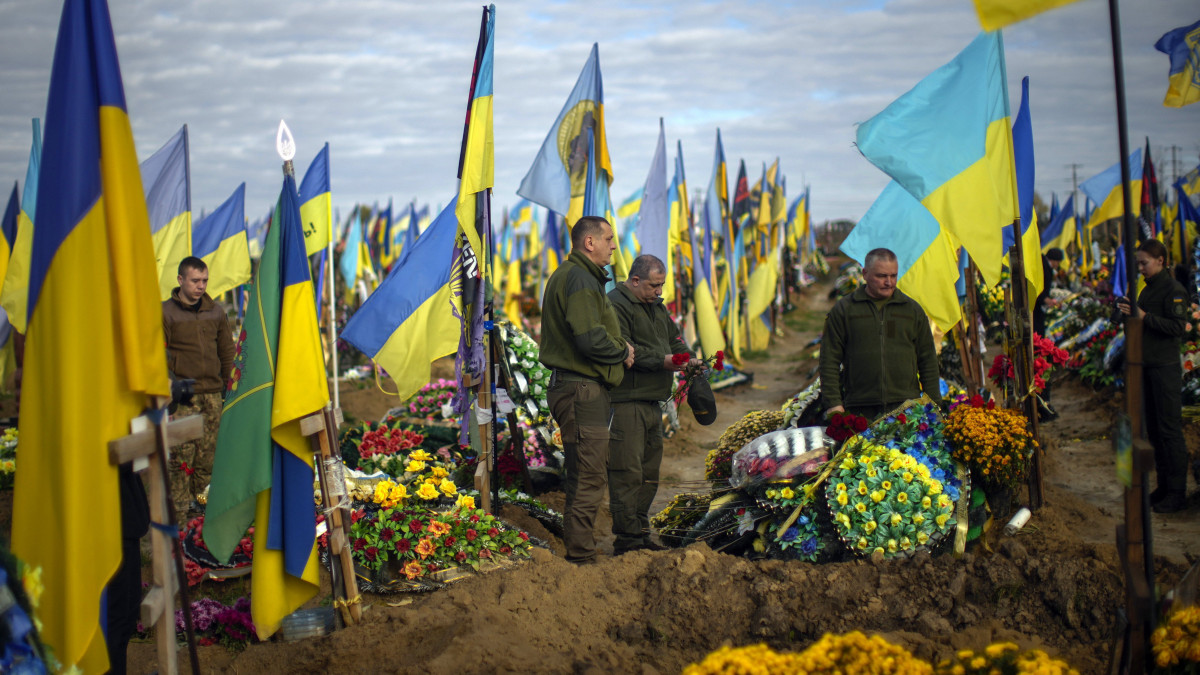 Az Ukrajna elleni orosz háborúban a közelmúltban elesett bajtársuk sírjára tesznek virágot ukrán katonák egy harkivi temetőben az ukrán honvédők napján, 2022. október 14-én.
