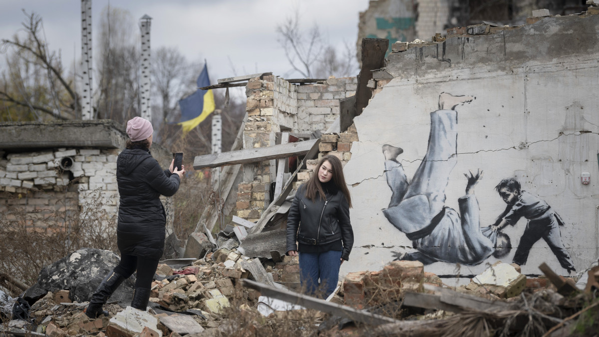 Fényképet készítő nők a háború során megrongálódott egyik épület falára festett alkotás előtt a Kijev közelében fekvő Borodjankában 2022. november 13-án. A falfestményt feltehetően Banksy brit graffitiművész készítette.